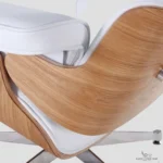 Macro detail of the ash wood veneer grain and white leather cushioning on an Eames style chair.